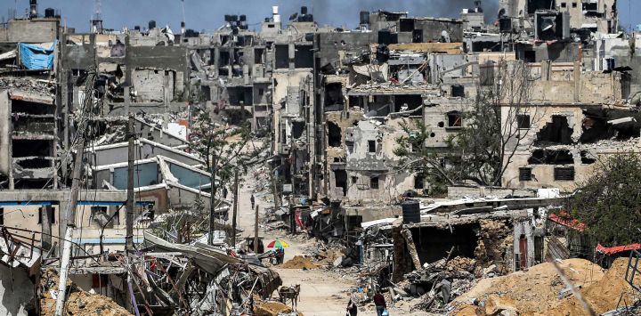 La gente pasa junto a edificios destruidos en Khan Yunis, en el sur de la Franja de Gaza, en medio del conflicto en curso en el territorio palestino entre Israel y el grupo militante Hamas.