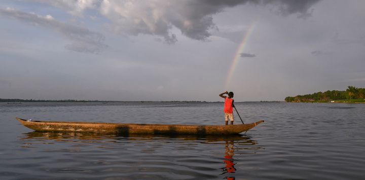 Una vista general de un arco iris mientras un joven se mueve en su piragua por el río Congo, República Democrática del Congo.