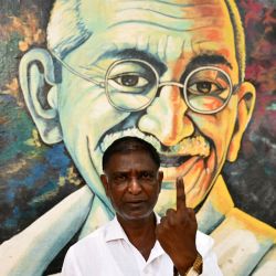 Joseph, un hombre de 54 años, posa para una fotografía frente a un mural del ícono de la libertad de la India, Mahatma Gandhi, mientras muestra su dedo entintado después de emitir su voto durante la segunda fase de la votación en las elecciones generales de la India, en Bengaluru. | Foto:IDREES MOHAMMED / AFP