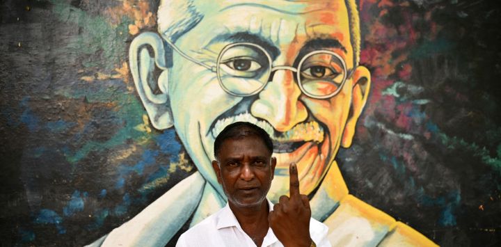 Joseph, un hombre de 54 años, posa para una fotografía frente a un mural del ícono de la libertad de la India, Mahatma Gandhi, mientras muestra su dedo entintado después de emitir su voto durante la segunda fase de la votación en las elecciones generales de la India, en Bengaluru.