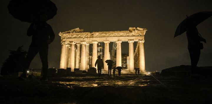 Los espectadores caminan frente al antiguo templo del Partenón en la cima de la colina de la Acrópolis antes del relevo de la antorcha olímpica en Atenas.