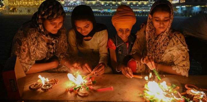 Devotos sij encienden velas en el Templo Dorado iluminado con motivo del aniversario del nacimiento de Guru Tegh Bahadur, en Amritsar, India.