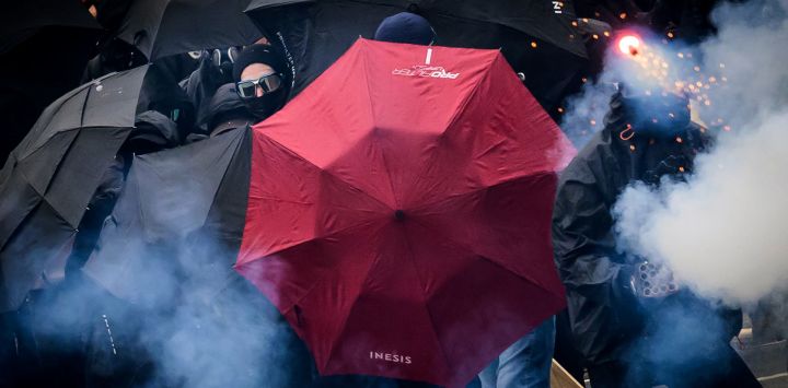 Los manifestantes se protegen detrás de paraguas abiertos mientras envían fuegos artificiales hacia la policía antidisturbios francesa durante una manifestación, que conmemora el Día Internacional de los Trabajadores, en Nantes, oeste de Francia.