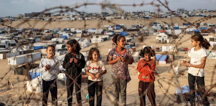 Niños se encuentran detrás de un alambre de púas a lo largo de una pendiente cerca de un campamento que alberga a palestinos desplazados en Rafah, en el sur de la Franja de Gaza, en medio del conflicto en curso en el territorio palestino entre Israel y el grupo militante Hamas.
