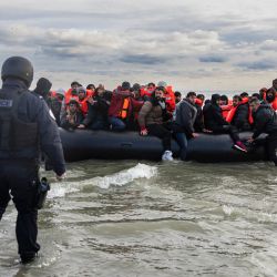 Los inmigrantes reaccionan mientras un oficial de policía francés está listo para perforar el barco del contrabandista con un cuchillo para evitar que los inmigrantes se embarquen en un intento de cruzar el Canal de la Mancha en la playa de Gravelines, cerca de Dunkerque, al norte de Francia. | Foto:SAMEER Al-DOUMY / AFP