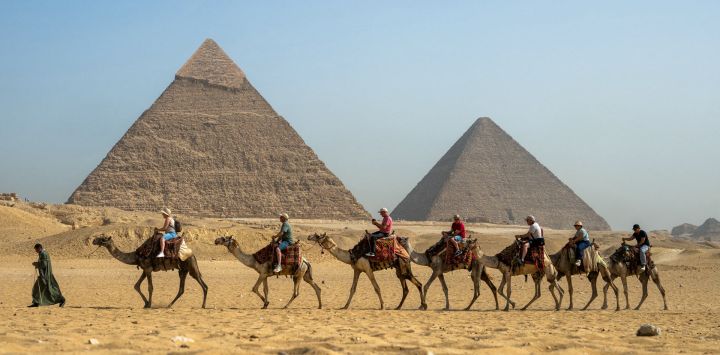 Un guía tira de un camello mientras los turistas pasan en fila pasando por la Gran Pirámide de Keops y la Pirámide de Khafre en la Necrópolis de las Pirámides de Giza en las afueras de Giza.