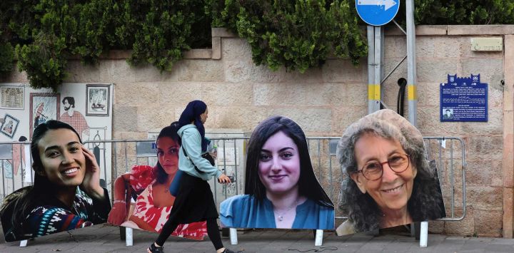Una mujer pasa junto a grandes retratos recortados de cartón de mujeres israelíes rehenes en Gaza desde los ataques del 7 de octubre, creados por familiares y simpatizantes durante una protesta pidiendo su liberación frente a la residencia del Primer Ministro en Jerusalén.