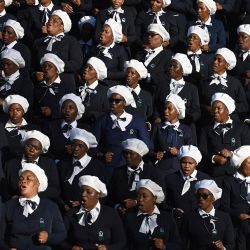 Miembros del coro de la Iglesia Cristiana de Sión (ZCC) cantan durante la ceremonia fúnebre de las víctimas de un accidente de autobús en el complejo deportivo Molepolole en Molepolole, Sudáfrica. | Foto:Monirul Bhuiyan / AFP