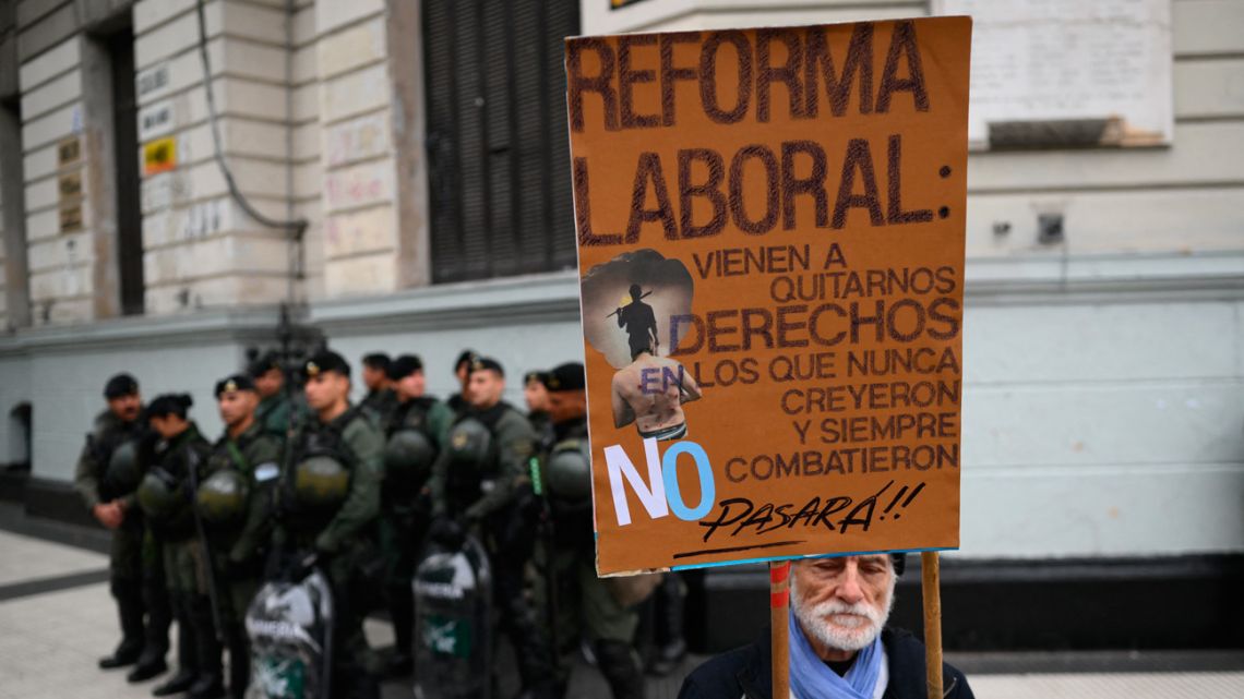 A man holds a placard against labour reform next to riot police as members of labour and social organisations march during a May Day (Labour Day) demonstration in Buenos Aires on May 1, 2024.