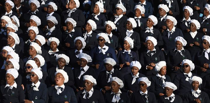 Miembros del coro de la Iglesia Cristiana de Sión (ZCC) cantan durante la ceremonia fúnebre de las víctimas de un accidente de autobús en el complejo deportivo Molepolole en Molepolole, Sudáfrica.