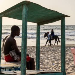 Un joven mira a una mujer dando un paseo a caballo por una playa en Banjul, Gambia. | Foto:JOHN WESSELS / AFP