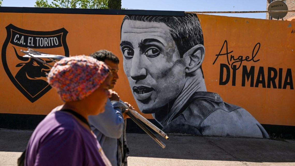 People walk past a mural of the local football legend Ángel Di María at a pitch of the El Torito football club, where the Argentina star began his career in Rosario, Argentina, on October 21, 2022. 