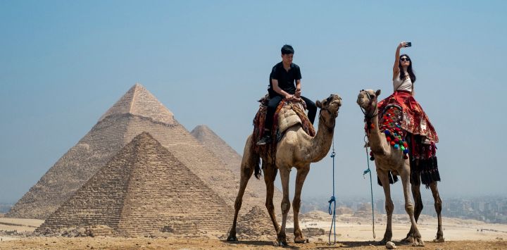 Un turista se toma una selfie mientras monta en camello en la Necrópolis de las Pirámides de Giza, en las afueras de Giza, Egipto.