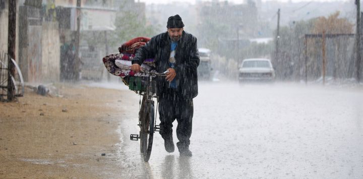 Un palestino desplazado empuja una bicicleta con sus pertenencias bajo la lluvia en Rafah, en el sur de la Franja de Gaza.
