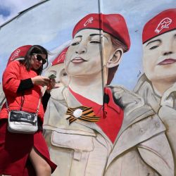 Una mujer usa su teléfono inteligente mientras pasa junto a un mural que representa a miembros del movimiento patriótico juvenil Yunarmiya (Ejército Joven) de Rusia en Moscú. | Foto:NATALIA KOLESNIKOVA / AFP
