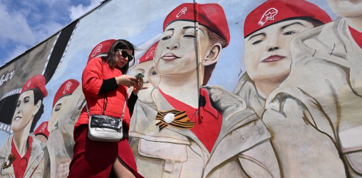 Una mujer usa su teléfono inteligente mientras pasa junto a un mural que representa a miembros del movimiento patriótico juvenil Yunarmiya (Ejército Joven) de Rusia en Moscú.