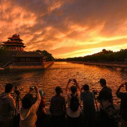 La gente toma fotografías de una torre cerca de la Ciudad Prohibida durante la puesta de sol en Beijing, China. | Foto:JADE GAO / AFP