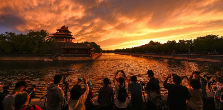 La gente toma fotografías de una torre cerca de la Ciudad Prohibida durante la puesta de sol en Beijing, China.