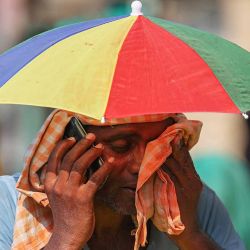 Un vendedor con un paraguas sobre la cabeza habla por teléfono móvil mientras se limpia la cara con un paño en un caluroso día de verano. Foto Niharika KULKARNI / AFP | Foto:AFP