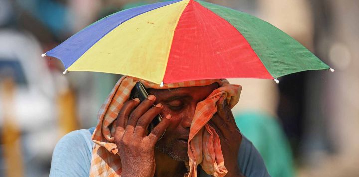 Un vendedor con un paraguas sobre la cabeza habla por teléfono móvil mientras se limpia la cara con un paño en un caluroso día de verano. Foto Niharika KULKARNI / AFP