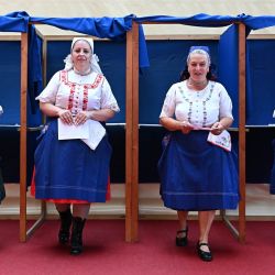 Mujeres con vestidos tradicionales húngaros abandonan la cabina de votación en un colegio electoral en una escuela en Veresegyhaz, a unos 30 kilómetros al este de Budapest, durante las elecciones para elegir sus representantes al Parlamento Europeo. | Foto:ATILA KISBENEDEK / AFP