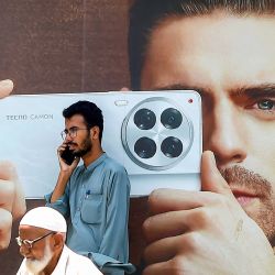 Un hombre asiste a una llamada telefónica frente a un anuncio móvil exhibido a lo largo de una calle en Karachi, Pakistán. | Foto:RIZWAN TABASSUM / AFP