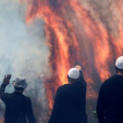 Hombres drusos locales observan las llamas que queman un campo después de que cohetes lanzados desde el sur del Líbano aterrizaran en el área de Banias en los Altos del Golán anexados por Israel, en medio de enfrentamientos transfronterizos en curso entre tropas israelíes y combatientes de Hezbolá. | Foto:JALAA MAREY / AFP