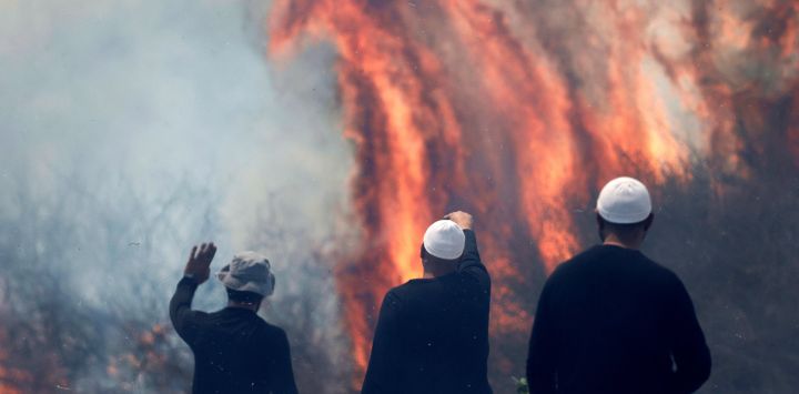 Hombres drusos locales observan las llamas que queman un campo después de que cohetes lanzados desde el sur del Líbano aterrizaran en el área de Banias en los Altos del Golán anexados por Israel, en medio de enfrentamientos transfronterizos en curso entre tropas israelíes y combatientes de Hezbolá.