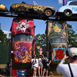 Los asistentes al festival posan para una foto frente a la instalación de arte Carhenge el día inaugural del festival de Glastonbury en Worthy Farm en el pueblo de Pilton en Somerset, suroeste de Inglaterra. | Foto:OLI SCARFF / AFP
