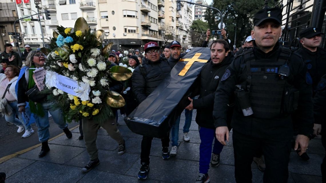 Demonstrators carry a cardboard coffin with flowers and a sign that reads 'Democracy' in front of the National Congress building during a protest as deputies attend a plenary session in Buenos Aires on June 27, 2024.  Deputies examine and vote on Senate changes to the economic reform package of President Javier Milei. 