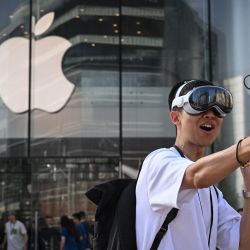 Un hombre que lleva un casco Apple Vision Pro graba imágenes mientras la gente espera para entrar a la Apple Store durante el lanzamiento del casco de realidad mixta en Beijing. | Foto:JADE GAO / AFP