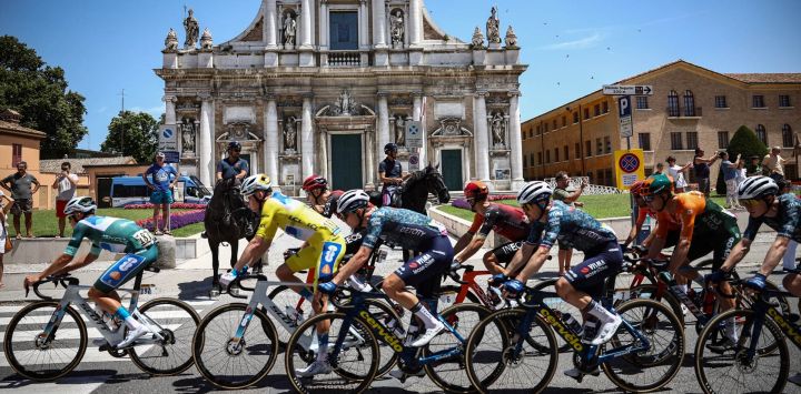 El ciclista francés del equipo DSM-Firmenich PostNL, Romain Bardet, vistiendo el maillot amarillo de líder general, recorre con el pelotón pasando por la Basílica de Santa María en Oporto, en la ciudad de Rávena, durante la 2.o etapa de la 111ª edición de la carrera ciclista Tour de Francia, 199 km entre Cesenatico y Bolonia, en Italia.