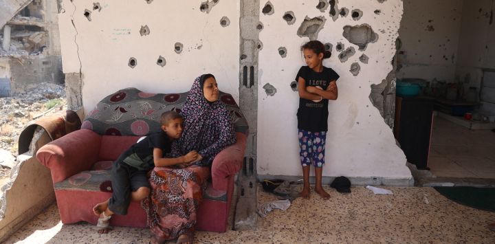 Un niño palestino abraza a una mujer y ella habla con una niña mientras está sentado en el balcón de una casa dañada en un bombardeo israelí, mientras algunos residentes regresan a la ciudad de Khan Yunis, en el sur de la Franja de Gaza, en medio de la conflicto en curso entre Israel y el grupo militante palestino Hamas.