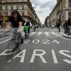 Los ciclistas pasan por encima de una señal de tráfico de un carril "París 2024" para los próximos Juegos Olímpicos de París 2024 a lo largo de la Rue de Rivoli, en París. | Foto:JULIEN DE ROSA / AFP