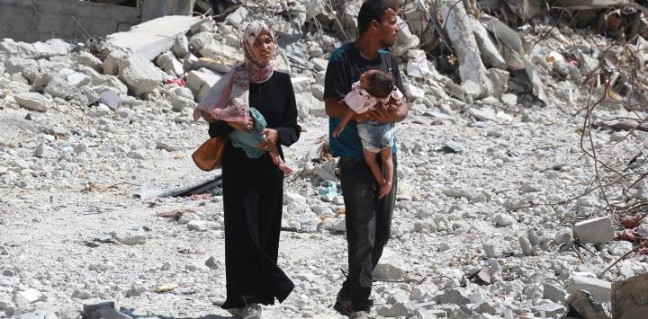 Una pareja palestina sostiene a sus hijos mientras caminan entre escombros en Khan Yunis, en el sur de la Franja de Gaza, en medio del conflicto en curso entre Israel y el grupo militante palestino Hamas.