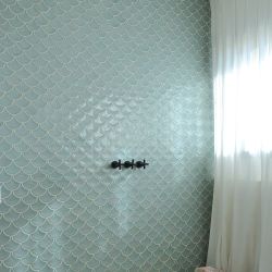 La pared de la ducha es de azulejos en verde agua y grifería negra.