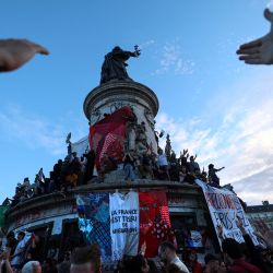 Los participantes hacen un gesto hacia una pancarta gigante que dice "Francia es el tejido de la migración" durante un mitin la noche electoral tras los primeros resultados de la segunda vuelta de las elecciones legislativas de Francia, en la Place de la Republique en París. | Foto:EMMANUEL DUNAND / AFP