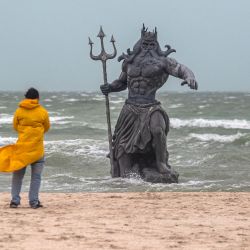 Un hombre mira una estatua del dios griego Poseidón en una playa durante el paso de la tormenta tropical Beryl en Progreso, en la Península de Yucatán, México. | Foto:HUGO BORGES / AFP