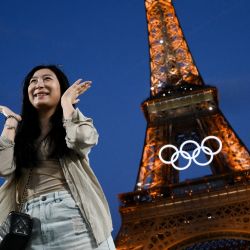 Una mujer posa frente a la Torre Eiffel con los anillos olímpicos expuestos antes de los Juegos Olímpicos y Paralímpicos de París 2024, en París. | Foto:LUIS ROBAYO / AFP