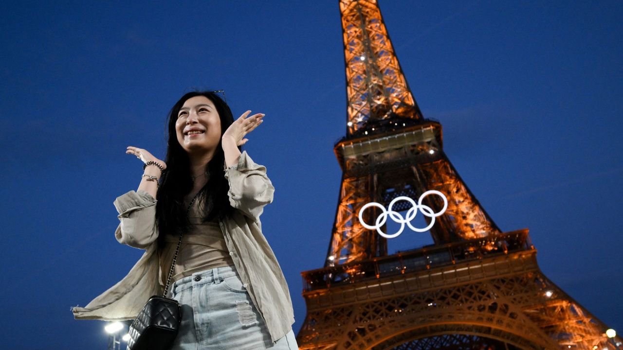 Una mujer posa frente a la Torre Eiffel con los anillos olímpicos expuestos antes de los Juegos Olímpicos y Paralímpicos de París 2024, en París. | Foto:LUIS ROBAYO / AFP