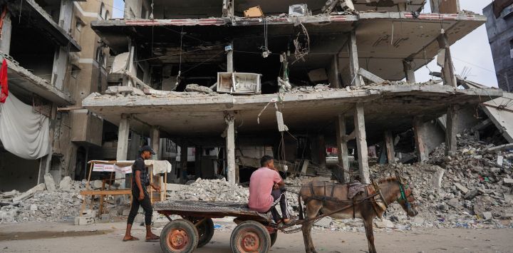 Palestinos desplazados viajan en un carro tirado por un burro pasando por edificios destruidos en Khan Yunis, en el sur de la Franja de Gaza, en medio del conflicto en curso entre Israel y el grupo militante palestino Hamas.
