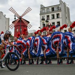 El ciclista francés Valentin Madouas pasa en bicicleta junto a bailarines del Moulin Rouge que realizan el cancán durante la carrera de ciclismo en ruta masculina durante los Juegos Olímpicos de París 2024 en París. | Foto:MAURO PIMENTEL / AFP