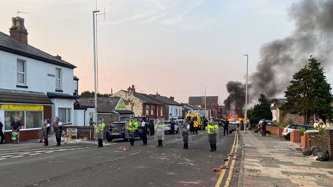 Smoke billows from a fire started by protesters as riot police stand guard after disturbances near the Southport Islamic Society Mosque in Southport, northwest England, on July 30, 2024.