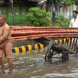Imagen de personas transportando bambúes mientras vadean a través del agua de la inundación en una calle después de las fuertes lluvias de monzón, en Lahore, Pakistán. | Foto:Xinhua/Sajjad