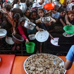 Palestinos, en su mayoría niños, extienden sus platos hacia un hombre para recibir su porción de hamburguesas de verduras preparadas por voluntarios en Beit Lahia, en el norte de la Franja de Gaza, en medio del conflicto en curso entre Israel y el grupo militante Hamás. | Foto:OMAR AL-QATTAA / AFP