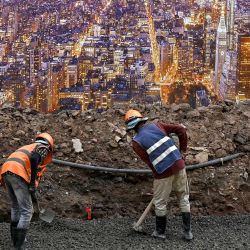 Los trabajadores de la construcción se preparan para construir los cimientos a lo largo de una calle junto a un cartel con una imagen de la ciudad de Nueva York en Phnom Penh, Camboya. | Foto:TANG CHHIN SOTHY / AFP