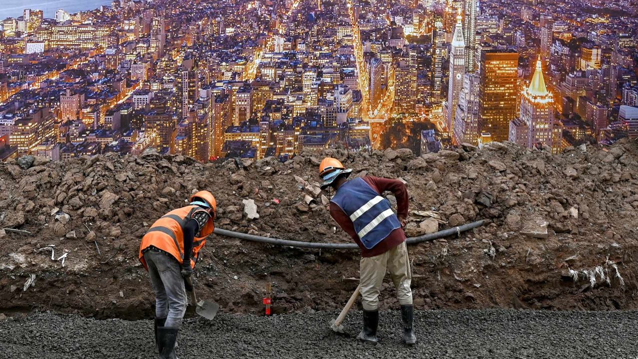 Los trabajadores de la construcción se preparan para construir los cimientos a lo largo de una calle junto a un cartel con una imagen de la ciudad de Nueva York en Phnom Penh, Camboya. | Foto:TANG CHHIN SOTHY / AFP