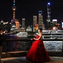 Una mujer posa para fotografías mientras la luna llena, también conocida como superluna azul, se eleva sobre los edificios del distrito financiero de Lujiazui en Shanghái. | Foto:Hector Retamal / AFP