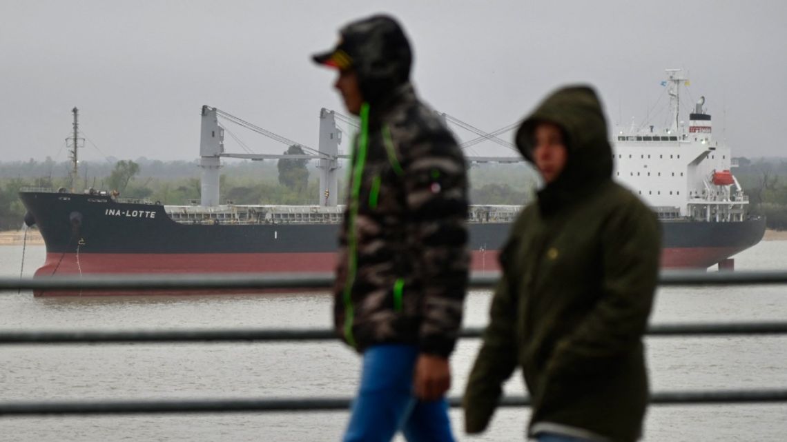 People walk in front of the bulk carrier 'Ina-Lotte' of Liberian flag anchored near San Lorenzo harbour, Santa Fe Province, Argentina, on August 21, 2024