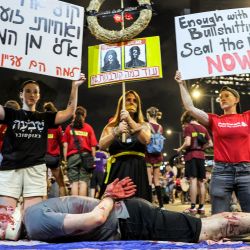 Un manifestante se hace pasar por un rehén israelí que yace en el suelo sobre una bandera mientras otros levantan carteles pidiendo un acuerdo durante una manifestación que exige acciones para liberar a los rehenes israelíes cautivos en la Franja de Gaza desde los ataques del 7 de octubre frente a la sede del Ministerio de Defensa israelí en Tel Aviv en medio del conflicto en curso en el territorio palestino entre Israel y Hamás. | Foto:JACK GUEZ / AFP